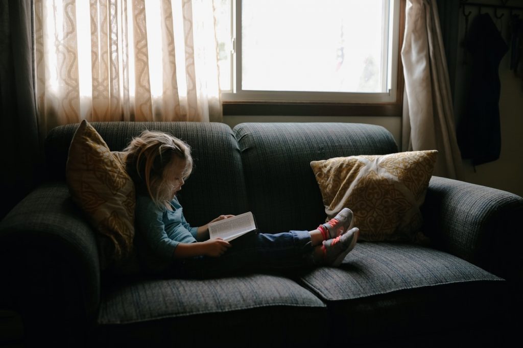 Uma criança lendo em um sofá como forma de passatempo.
