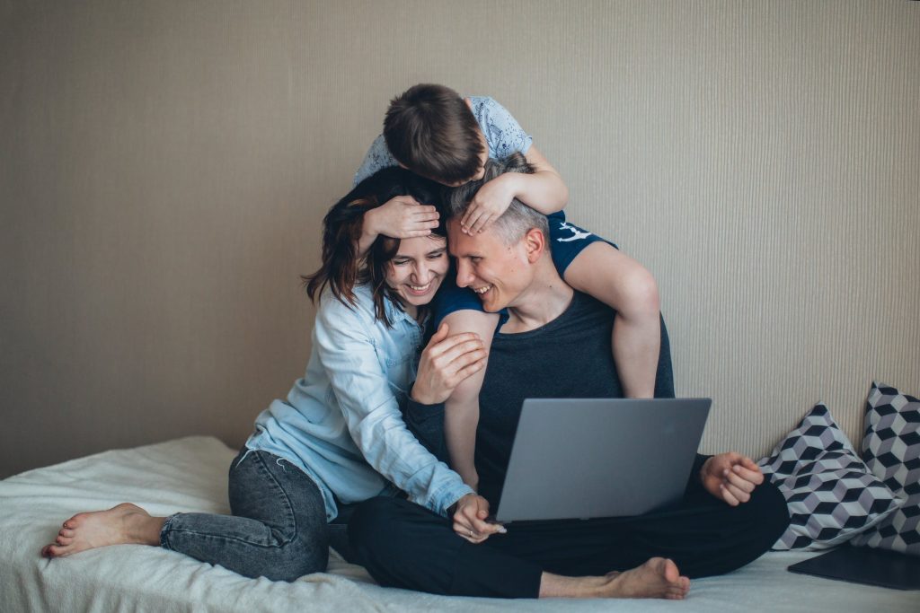 Pai, mãe e filho sentados, fazendo compras pela internet, enquanto se divertem.