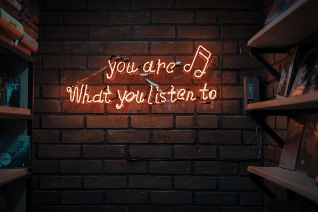 Parede de tijolos escrito em inglês em neon: "you are what you listen to". Tradução: "Você também é o que você ouve"