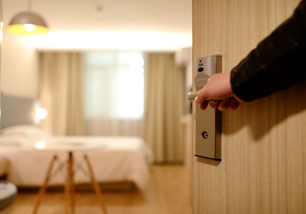 Na imagem há um indivíduo abrindo a porta de um quarto de hotel.