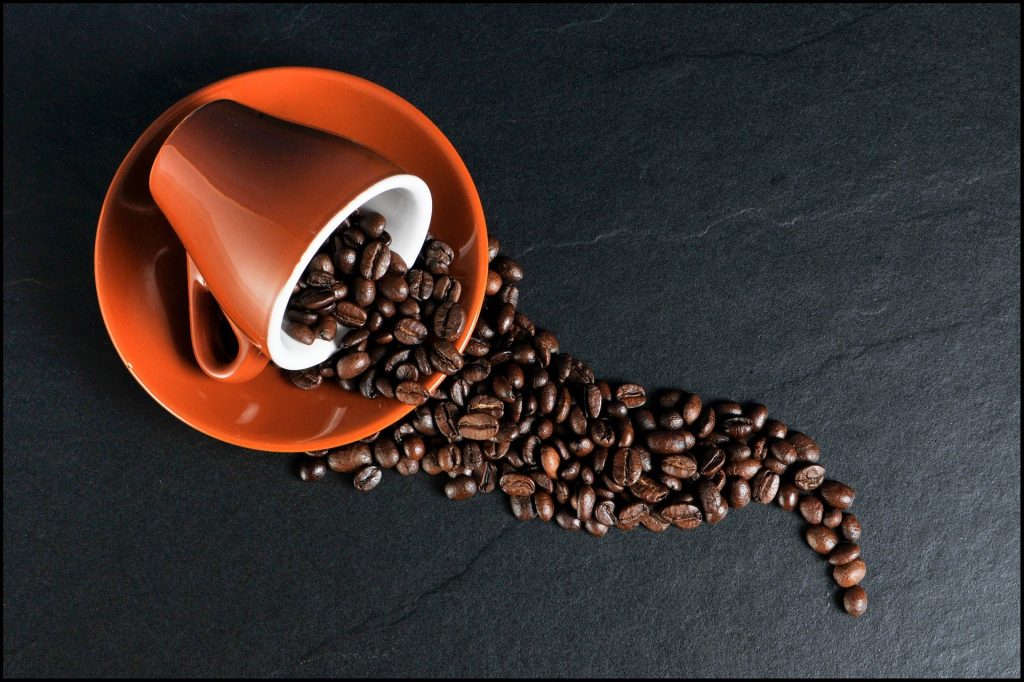 Na imagem há uma xícara deitada sobre o pires com grãos de café esparramando sobre o pires e uma bancada de granito.
