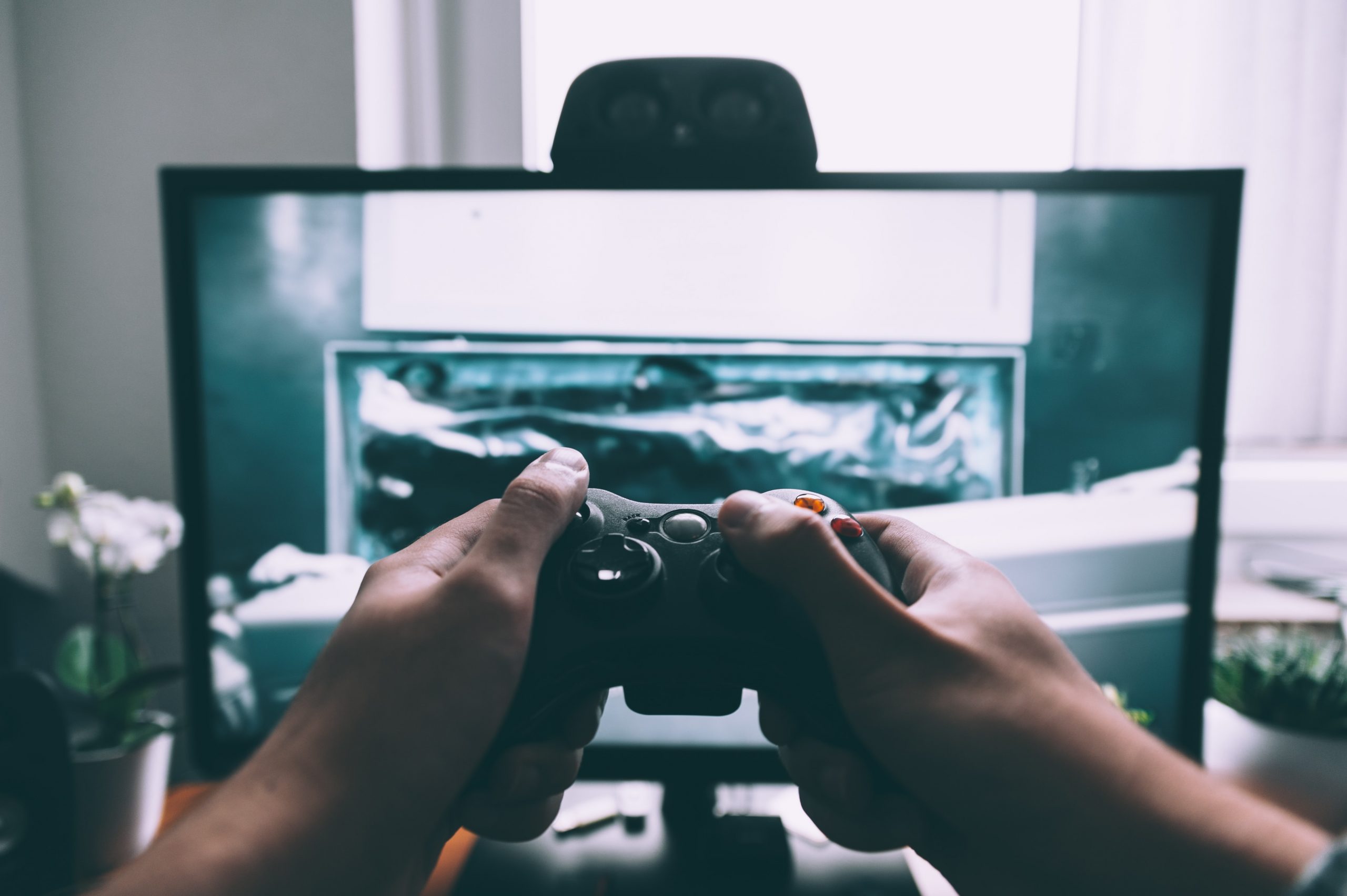 Na imagem há uma pessoa segurando um controle joystick com as duas mãos em frente à uma tela de computador com a imagem de um jogo.