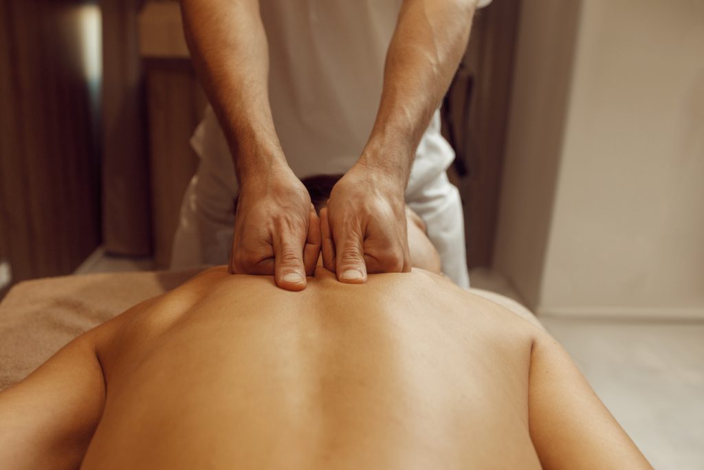 Pessoa recebendo massagem realizada por um homem utilizando a mão fechada e os polegares.