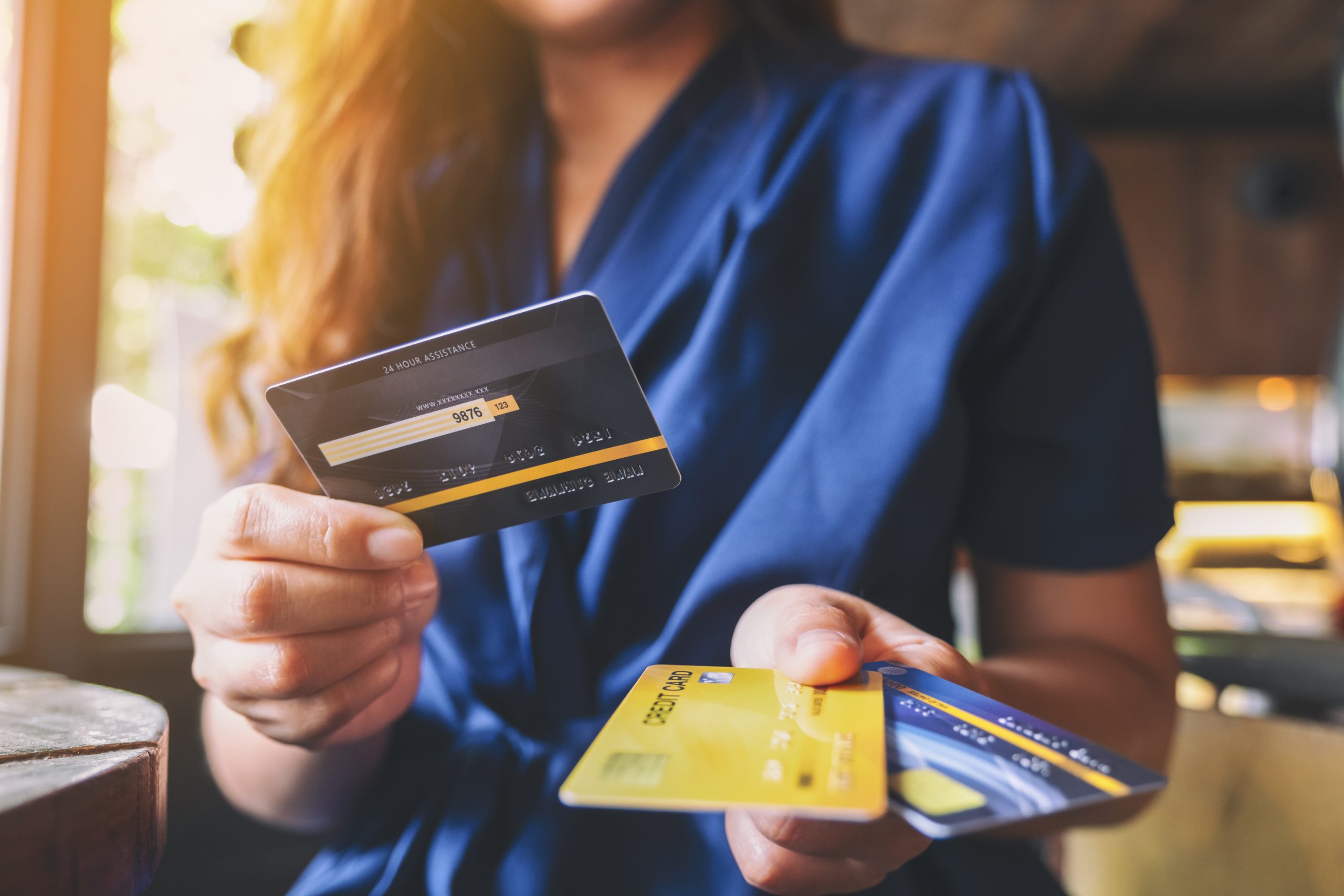 Mulher branca de pé utilizando uma roupa azul escuro está segurando um cartão de crédito com a mão esquerda e dois com a direita, ela está simulando uma transferência de ponto entre bancos.